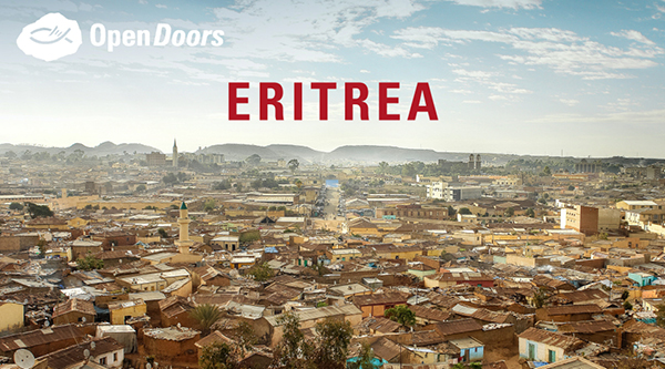 Blick auf eine Stadt in Eritrea mit vielen braun-beigen Häusern, Hügeln im Hintergrund und in rot Eritrea darüber