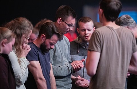 Junge Menschen stehen in einer Veranstaltungshalle zusammen und beten für verfolgte Christen