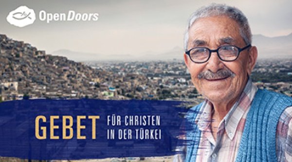 Ein lächelnder ältere Mann mit Brille, Karohemd und Weste ist vor einer Stadt in der Türkei