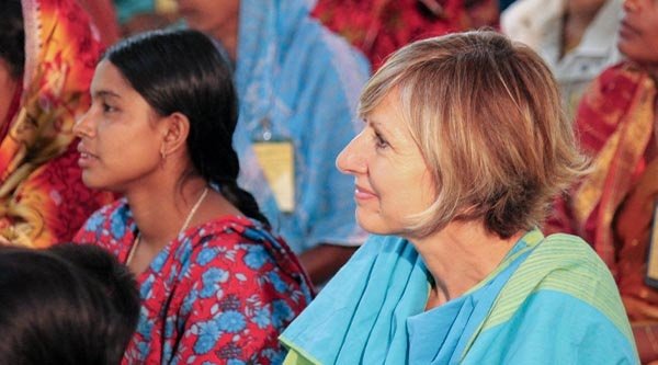 Eine hellhäutige Frau sitzt neben einer indischen Frau und beide haben ein traditionelles Gewand an. 