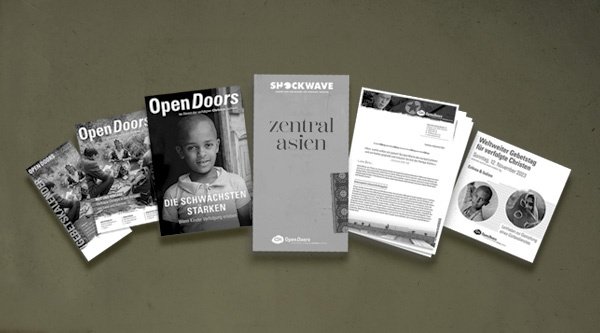Verschiedene Printmaterialien von Open Doors in grau vor einem grünen Hintergrund