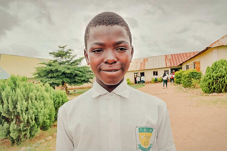 Junge aus Afrika in Schuluniform vor einem Gebäude