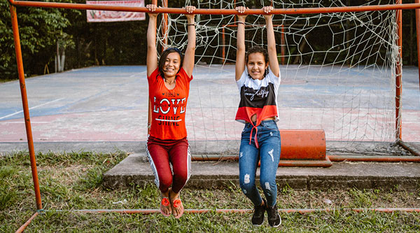 Zwei kolumbianische Mädchen lächeln an einer Sportstange baumelnd in die Kamera
