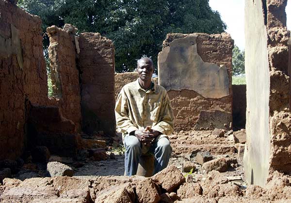 Afrikanischer Mann sitzt vor einem zerstörten Haus