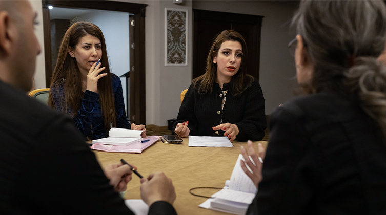 Drei Frauen in schwarzer Kleidung und ein Mann sitzen am Tisch mit Notizheften vor sich und Stiften in der Hand