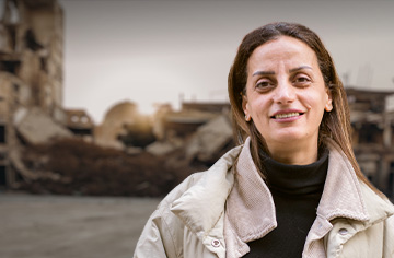 Syrische Frau mit zerstörten Gebäuden im Hintergrund