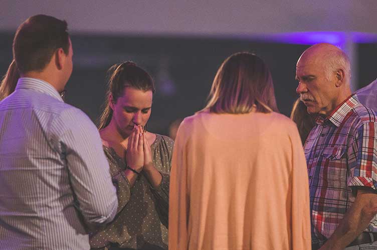 Eine Gruppe von Menschen gemischten Alterns steht zusammen im Gebet für verfolgte Christen