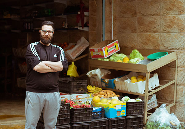 Ein Mann steht mit verschränkten Armen vor mehreren Regalen mit Obst und Gemüse