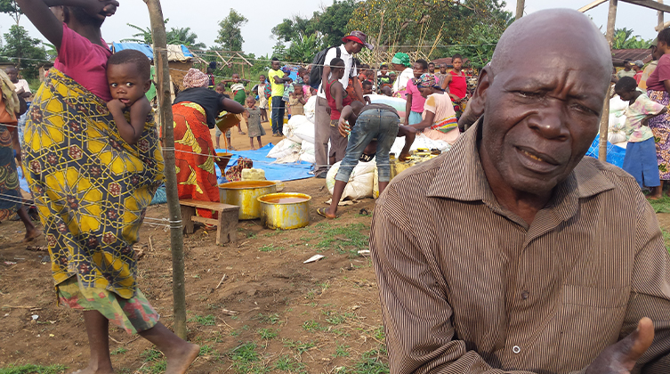 Im Vordergrung ein Kongolese mit kritischem Blick un dim Hintergrund viele Menschen, die gemeinsam essen 