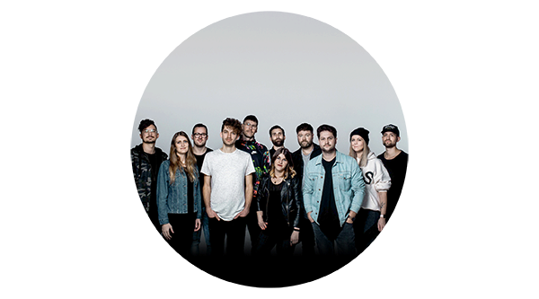 Eine Gruppe junge Leute mit Jeansjacke oder T-Shirt, schwarzen Hosen und hoher weißer Wand dahinter