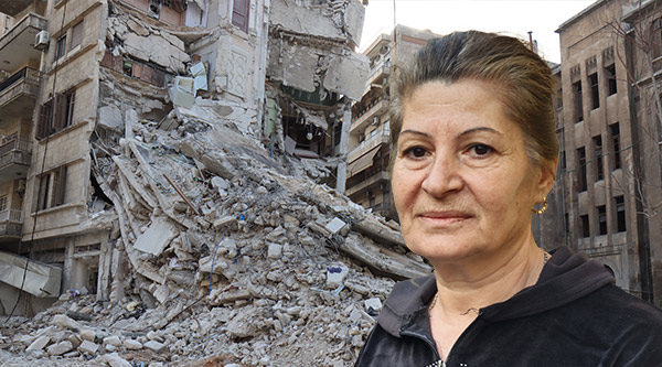 Eine syrische ältere Frau schaut in die Kamera. Hinter ihr die Trümmer eines Hauses nach dem Erdbeben.