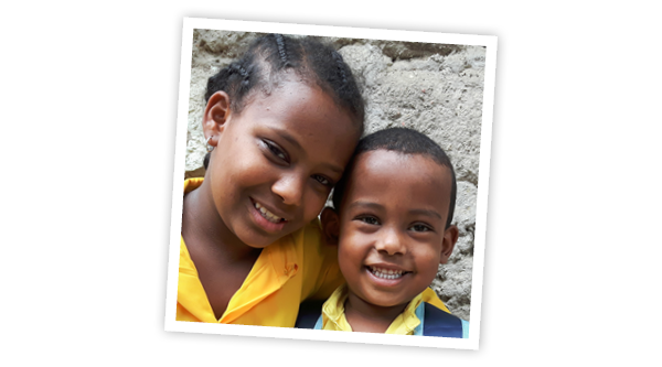 Zwei lächelnde afrikanische Kinder, das Mädchen hat den Arm um die Schulter des kleineren Jungen und beide haben ein gelbes Oberteil an
