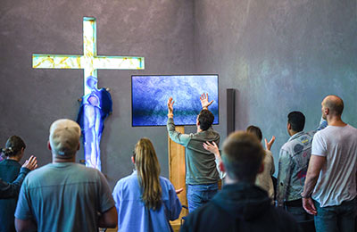 Eine Gruppe Menschen von hinten vor einem leuchtenden Kreuz mit erhobenen Händen