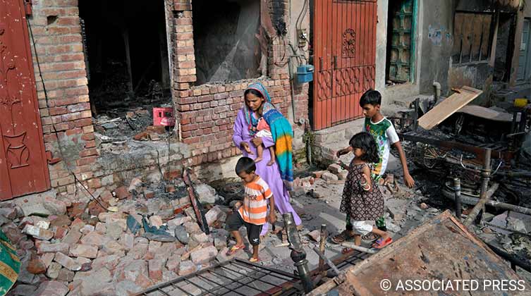 Eine Christin läuft mit ihren Kindern in Jaranwala (Provinz Punjab Ostpakistan) durch die Trümmer eines von einer aufgebrachten Menschenmenge zerstörten Hauses