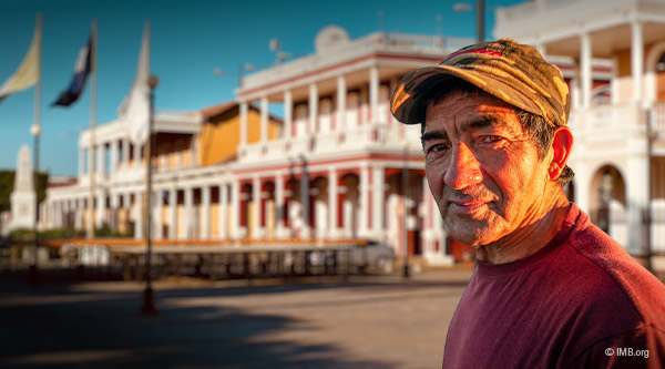 Ein älterer Mann aus Nicaragua mit rotem Pullover und Mütze steht vor einem Gebäude aus der Kolonialzeit 
