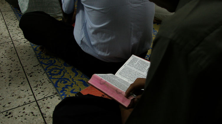 Eine sitzende Person seitlich hält ein aufgeschlagenes Buch in den Händen