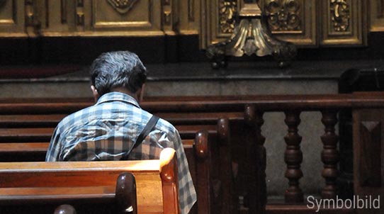 Ein Mann von hinten sitzt mit einer gebeugten Haltung auf einer Kirchenbank