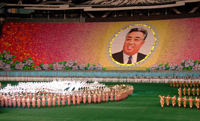 An der Wand in einem Stadion ist das portrait eines Mannes groß abgebildet. Auf der Rasenfläche davor befindet sich eine große Menschenmenge