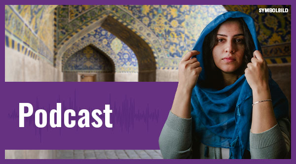 Eine Frau in einem iranischen Gebäude hält ihr Kopftuch mit den Händen fest