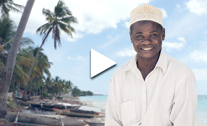 Eine Person in einem hellen Gewand steht am Strand vor Palmen