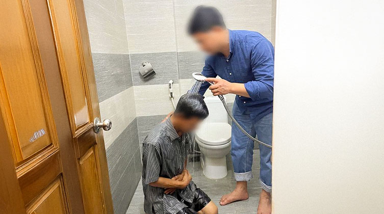 Ein Mann kniet auf dem Badezimmerboden und ein anderer hält eine Duschbrause über seinen Kopf
