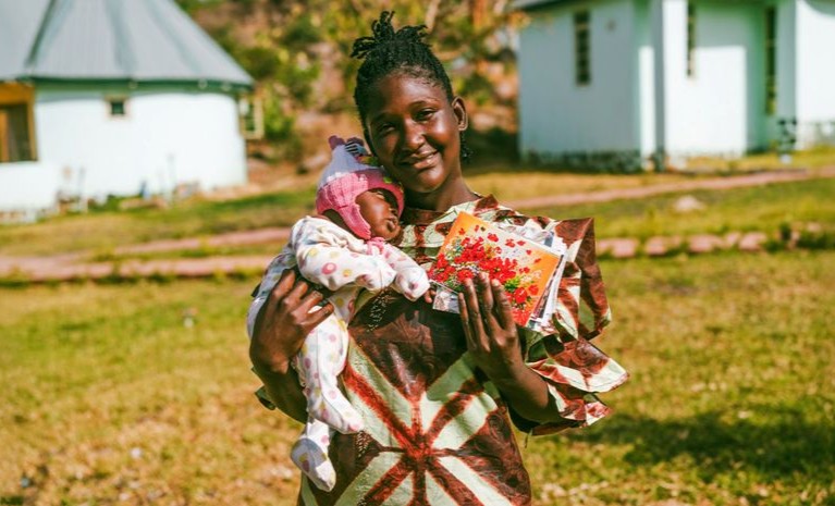 Eine Frau hält ihr Kind auf dem Arm. In der anderen Hand hält sie Ermutigungspost von Open Doors.