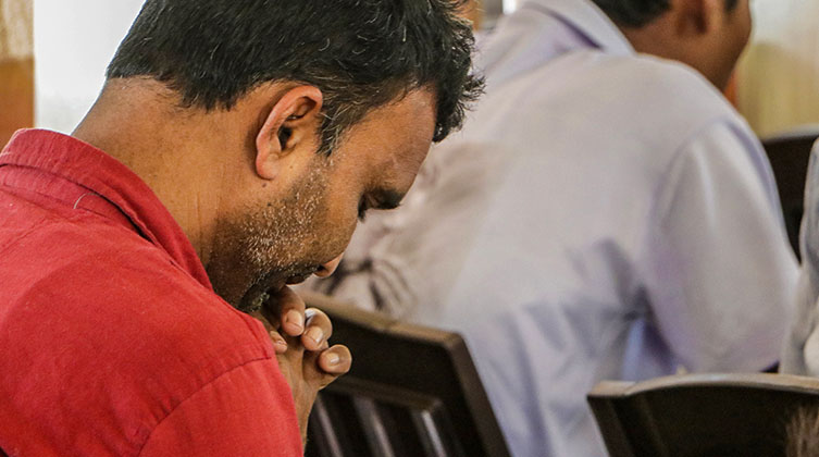 Mann mit rotem T-Shirt betet in einem Gottesdienst
