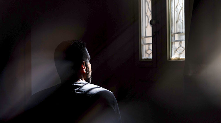 Ein Mann in einem dunklen Raum schaut aus einem Fenster
