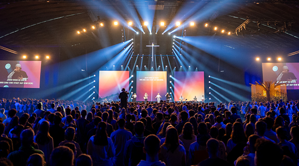 Tausende Jugendliche stehen im Lobpreis zusammen und feiern vor einer großen Bühne
