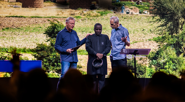 Zwei Männer beten auf einer Bühne für einen Mann aus Afrika 