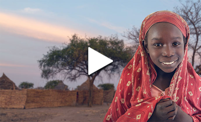 Ein afrikanisches Mädchen steht vor einem Dorf und lächelt