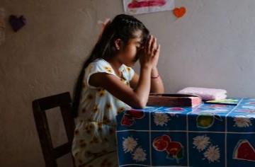 Ein junges Mädchen sitzt betend am Tisch