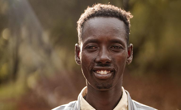 Ein dunkelhäutiger Mann vor einem unscharfen Wald im Hintergrund