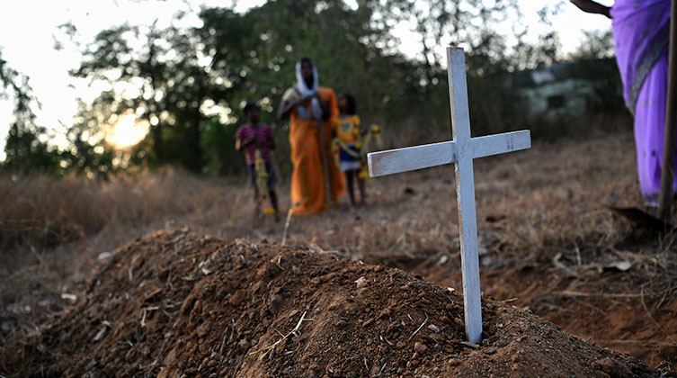 Ein paar Menschen stehen um ein Grab mit einem weißen Kreuz