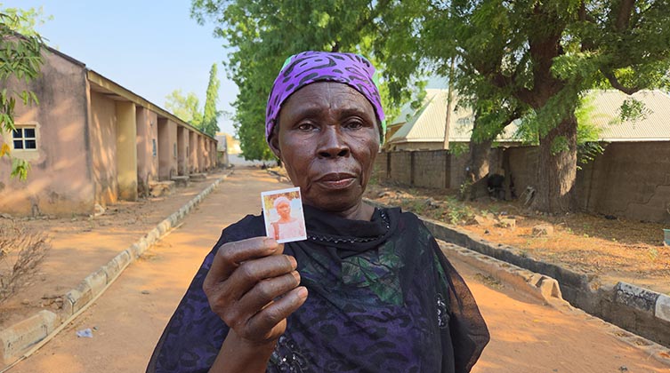 Porträt einer Frau mit dunkler Hautfarbe. Sie hält ein Foto in die Kamera.