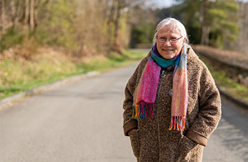 Eine Frau mit weißen Haaren steht im Wald und lächelt in die Kamera