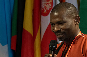 Ein Mann steht vor mehreren Flaggen und spricht in ein Mikrofon