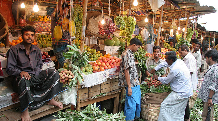 Mehrere Männer stehen an einem Marktstand voll mit Obst