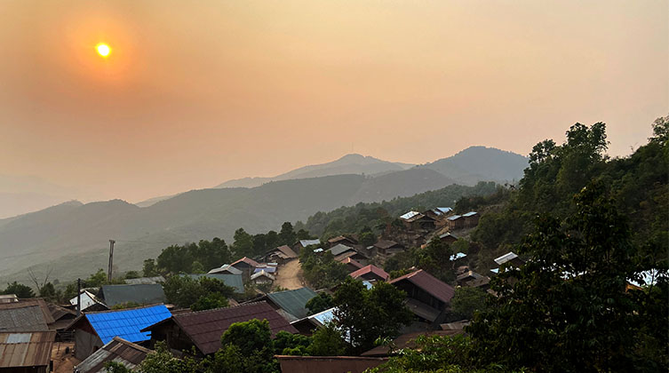 Eine Hügellandschaft bei Sonnenuntergang mit vielen Bäumen und ein paar kleinen Häusern