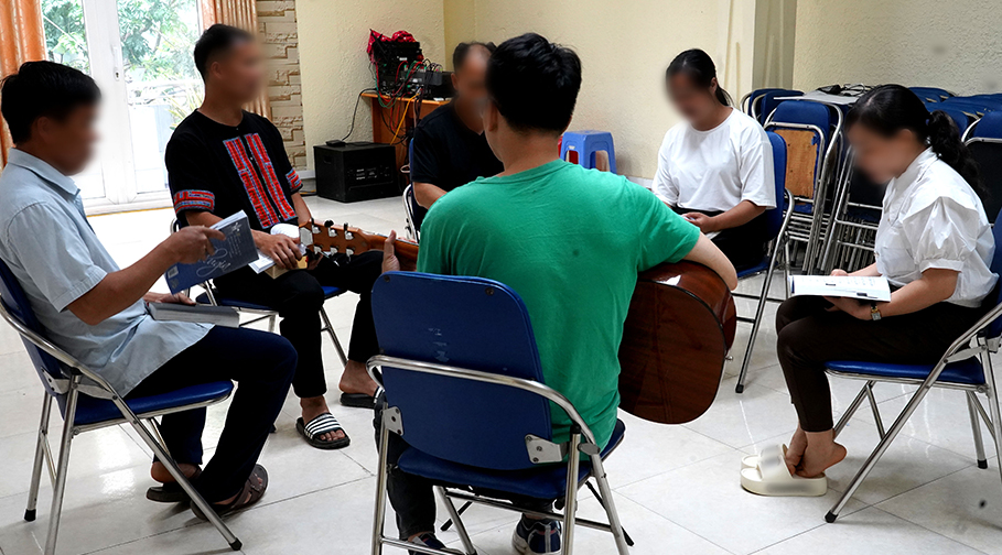 Junge Menschen sitzen im Kreis mit einer Gitarre