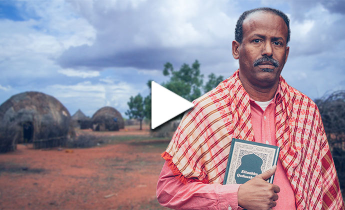 Ein Mann mit einem Buch in der Hand steht in einem afrikanischen Dorf