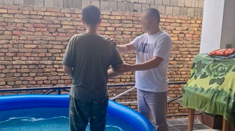 Ein Mann wird von einem anderen Mann in einem Pool getauft.
