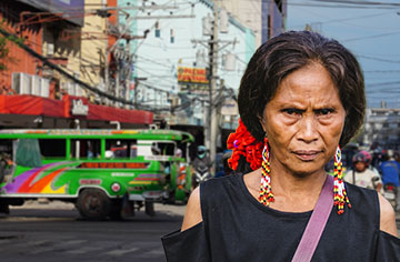 Eine ältere Frau steht an einer belebten Straßenkreuzung einer philippinschen Stadt