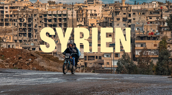 Schriftzug „SYRIEN“ vor einem Stadtbild im Nahen Osten
