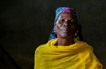 Eine afrikanische Frau in gelbem Gewand vor einem schwarzen Hintergrund.