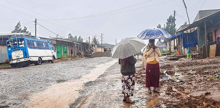 Zwei Frauen laufen im Regen auf einer matschigen Straße 