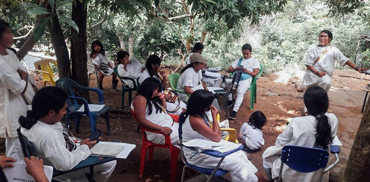 Eine Gruppe von indigenen Menschen sitzt unter Bäumen zusammen