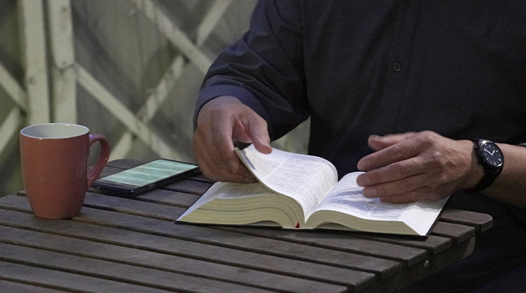 Eine Person sitzt mit einer Tasse und einer Bibel an einem Tisch