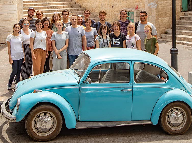 Eine Reisegruppe hinter einem blauen Käfer