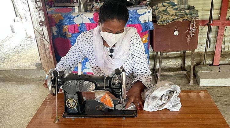 Indische Frau sitzt mit Mund-und Nasenschutz an einer Nähmaschine und arbeitet
